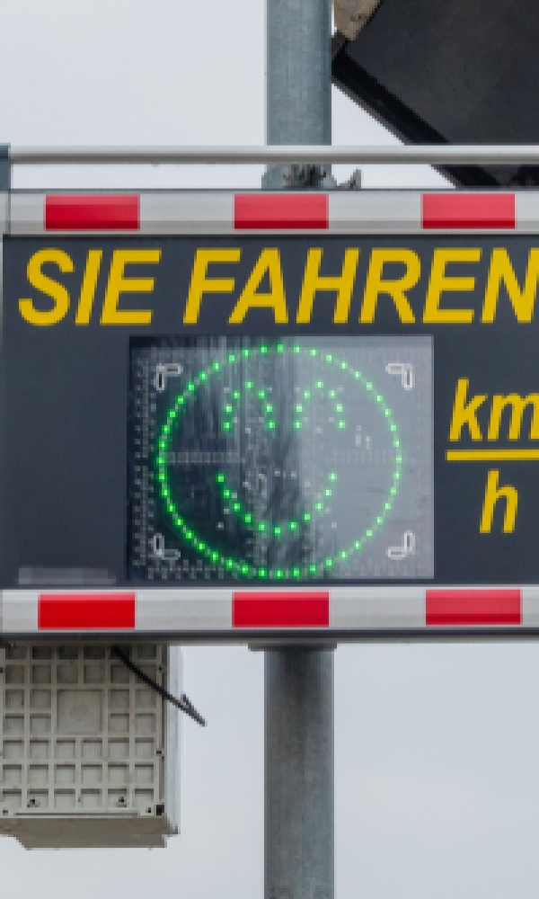 Ein Verkehrsschild mit der Anzeige „SIE FAHREN“ zeigt die Geschwindigkeit in km/h an. Auf dem Display ist ein grüner Smiley zu sehen, der korrektes Fahrverhalten signalisiert.