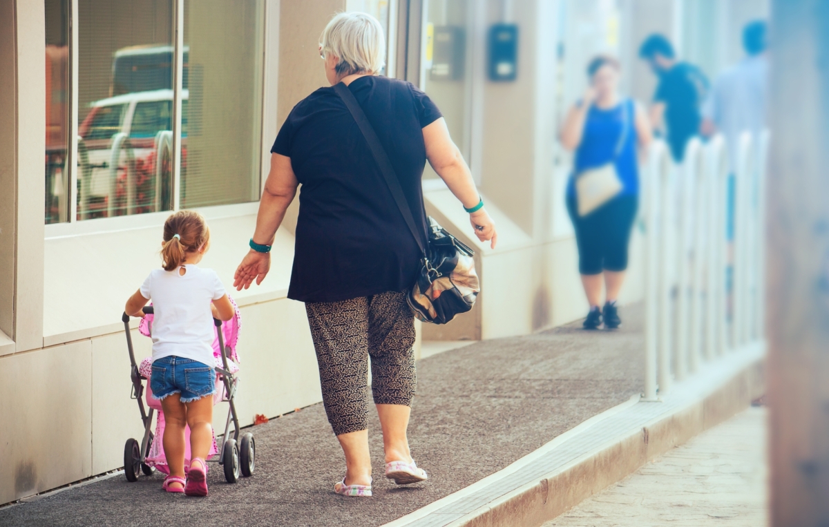 Kind mit Kinderwagen und Oma am Gehweg