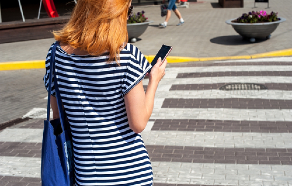 Frau überquert Zebrastreifen mit Handy in der Hand