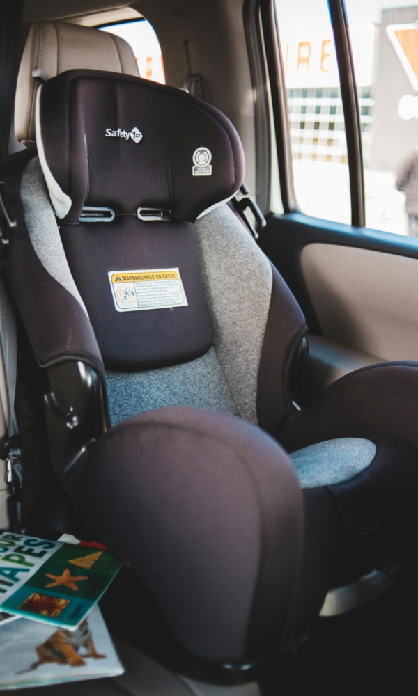 Ein Kindersitz ist in einem Auto installiert. Der Sitz ist schwarz-grau und steht auf dem Rücksitz. Neben der Tür ist ein Teil der Fensteröffnung zu sehen.