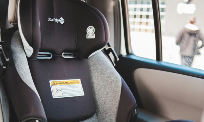 Ein Kindersitz ist in einem Auto installiert. Der Sitz ist schwarz-grau und steht auf dem Rücksitz. Neben der Tür ist ein Teil der Fensteröffnung zu sehen.