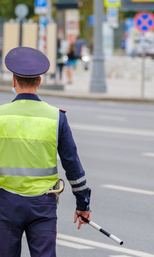 Ein Polizist in Uniform mit reflektierender Weste steht auf einer Straße und regelt den Verkehr.