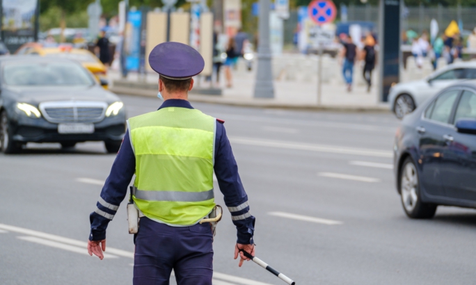Ein Polizist in Uniform mit reflektierender Weste steht auf einer Straße und regelt den Verkehr.