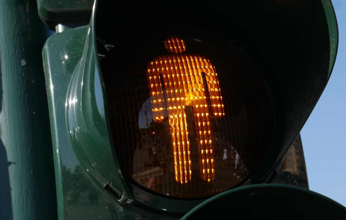 Gelbes Fußgängersignal einer Ampel in Form einer stehenden Person, das anzeigt, dass Fußgänger warten sollen.