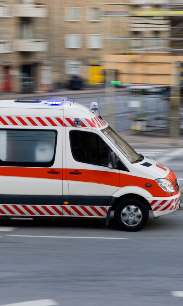 Ein Rettungswagen mit eingeschaltetem Blaulicht fährt schnell durch eine Stadtstraße.