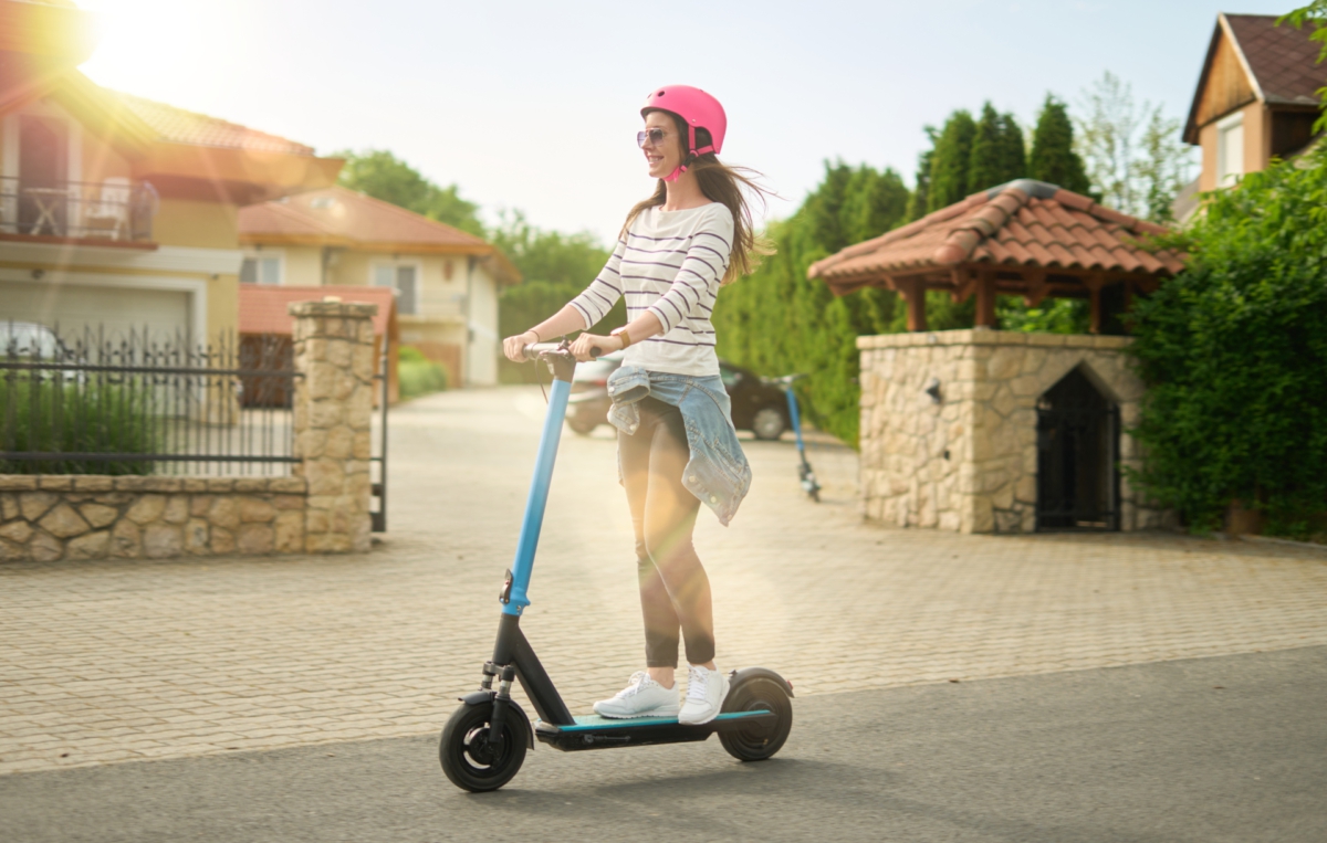 Junge Frau mit pinkem Helm fährt entspannt auf einem E-Scooter durch ein Wohngebiet.