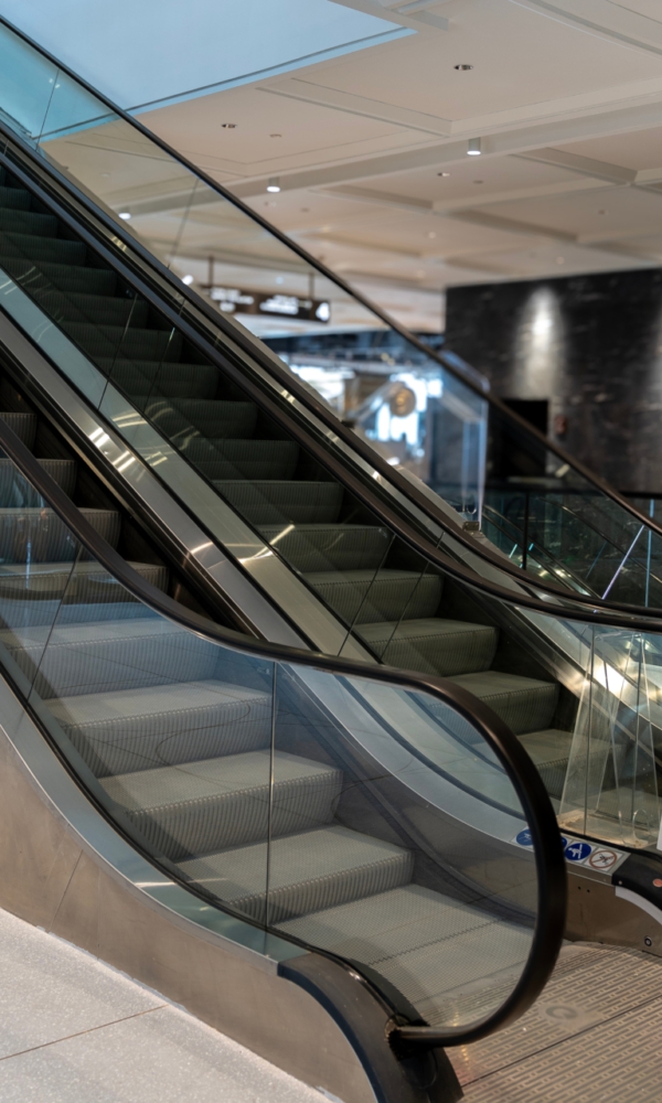 Leere Rolltreppe in einem modernen Einkaufszentrum oder Gebäude, mit Glasgeländern und metallischen Seitenwänden.