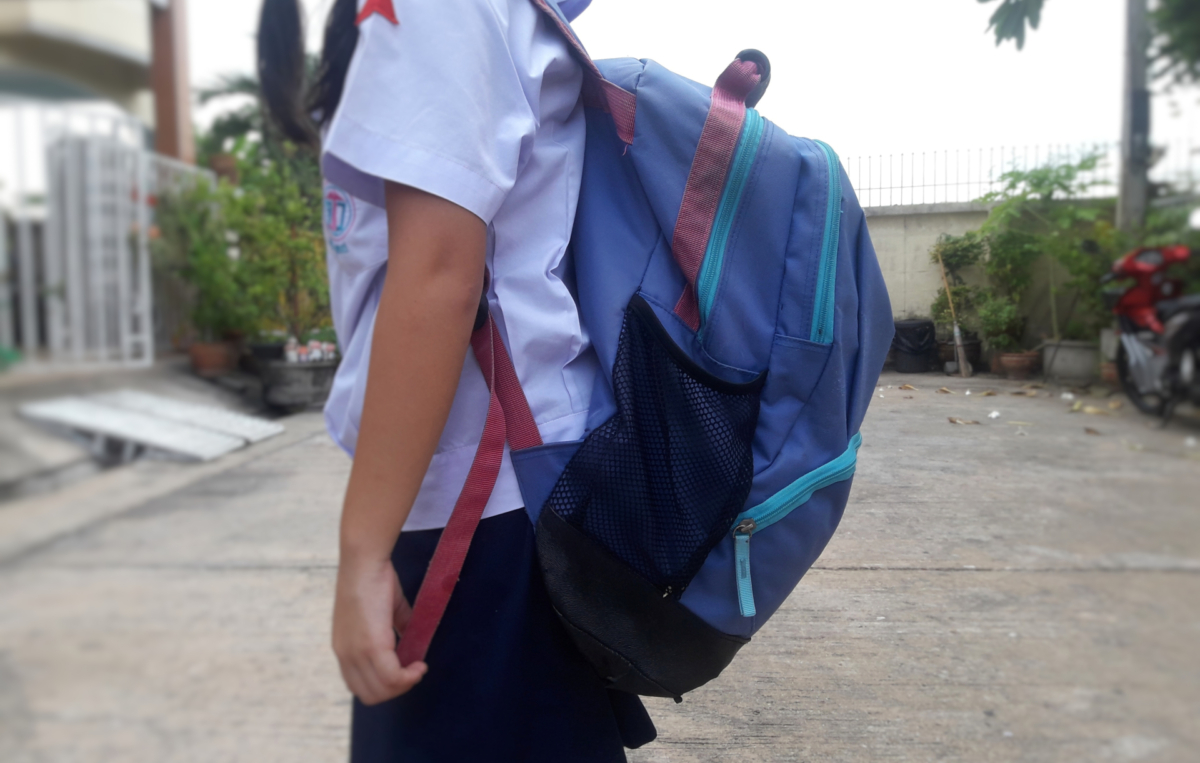 Ein Schulkind mit weißem Hemd und dunkelblauem Rock trägt einen großen blauen Rucksack.