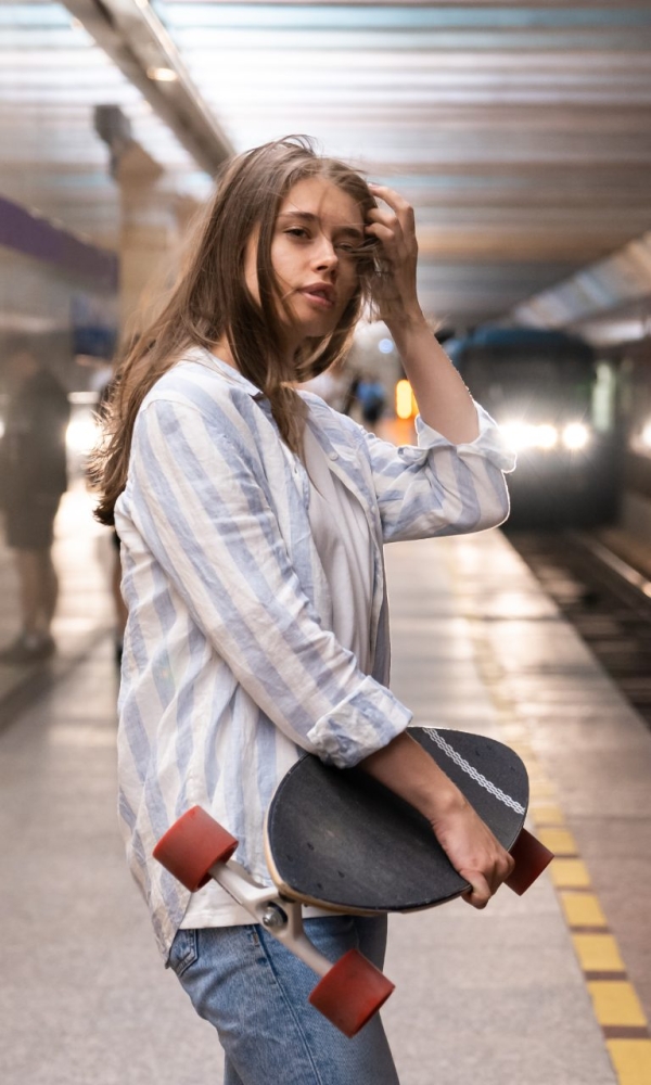 Mädchen steht mit einem Skateboard im Arm am Bahnsteig einer U-Bahn-Station, während ein Zug einfährt.