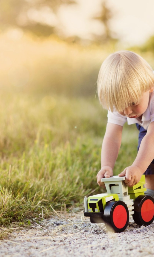 Ein kleines Kind spielt draußen auf einem Feldweg mit einem grünen Spielzeugtraktor mit roten Rädern.