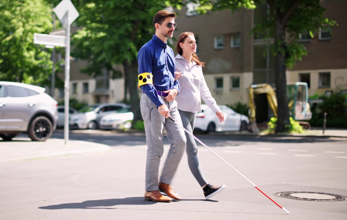 Blinder Mann überquert die Straße mit der Hilfe einer Frau