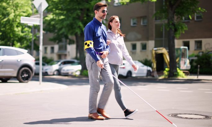 Blinder Mann überquert die Straße mit der Hilfe einer Frau