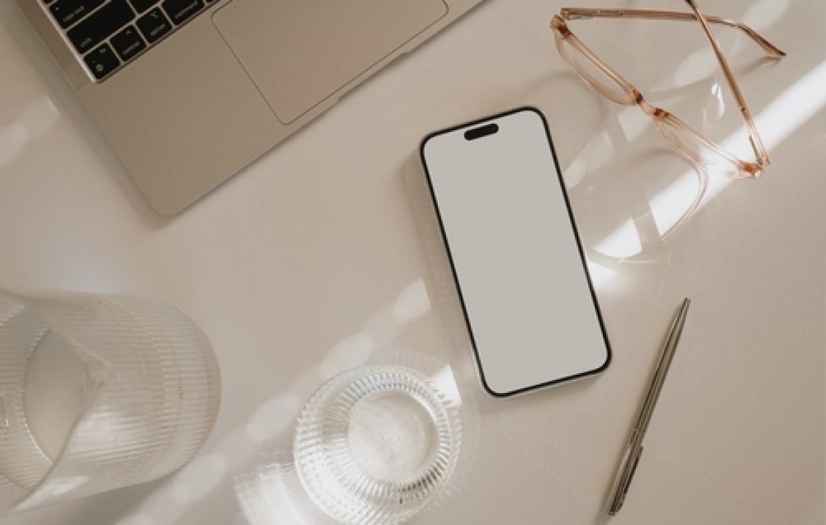 Smartphone liegt zwischen Laptop, Brille und Glas