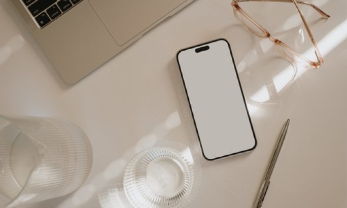 Smartphone liegt zwischen Laptop, Brille und Glas