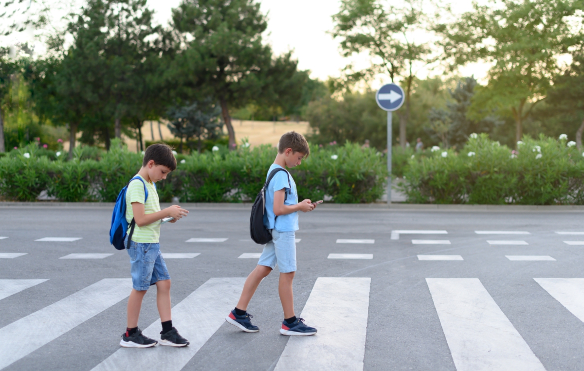 Zwei Jungen mit Rucksäcken überqueren einen Zebrastreifen, während sie auf ihre Smartphones schauen.
