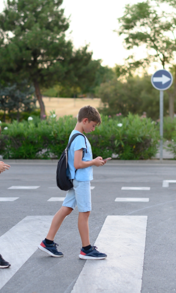 Zwei Jungen mit Rucksäcken überqueren einen Zebrastreifen, während sie auf ihre Smartphones schauen.