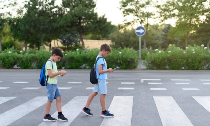 Zwei Jungen mit Rucksäcken überqueren einen Zebrastreifen, während sie auf ihre Smartphones schauen.