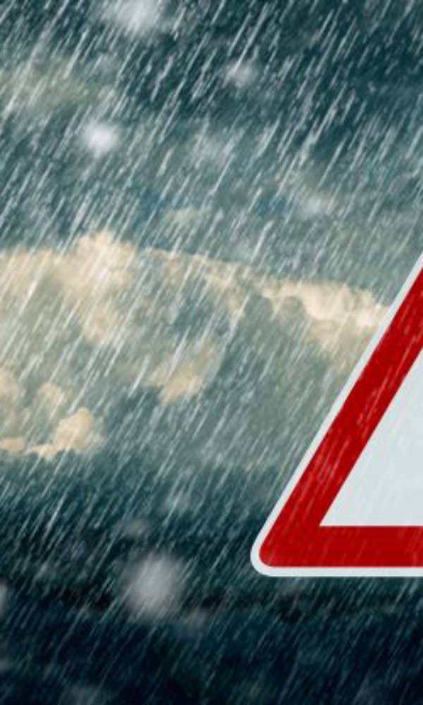 Verkehrsschild mit Ausrufezeichen als Warnhinweis, im Hintergrund starker Regen und dunkle Wolken.