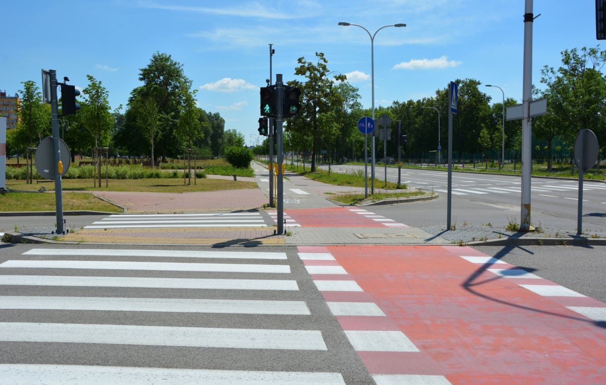 Fußgängerüberweg mit Zebrastreifen und Radweg, Verkehrsampeln und Radwegmarkierung bei sonnigem Wetter.