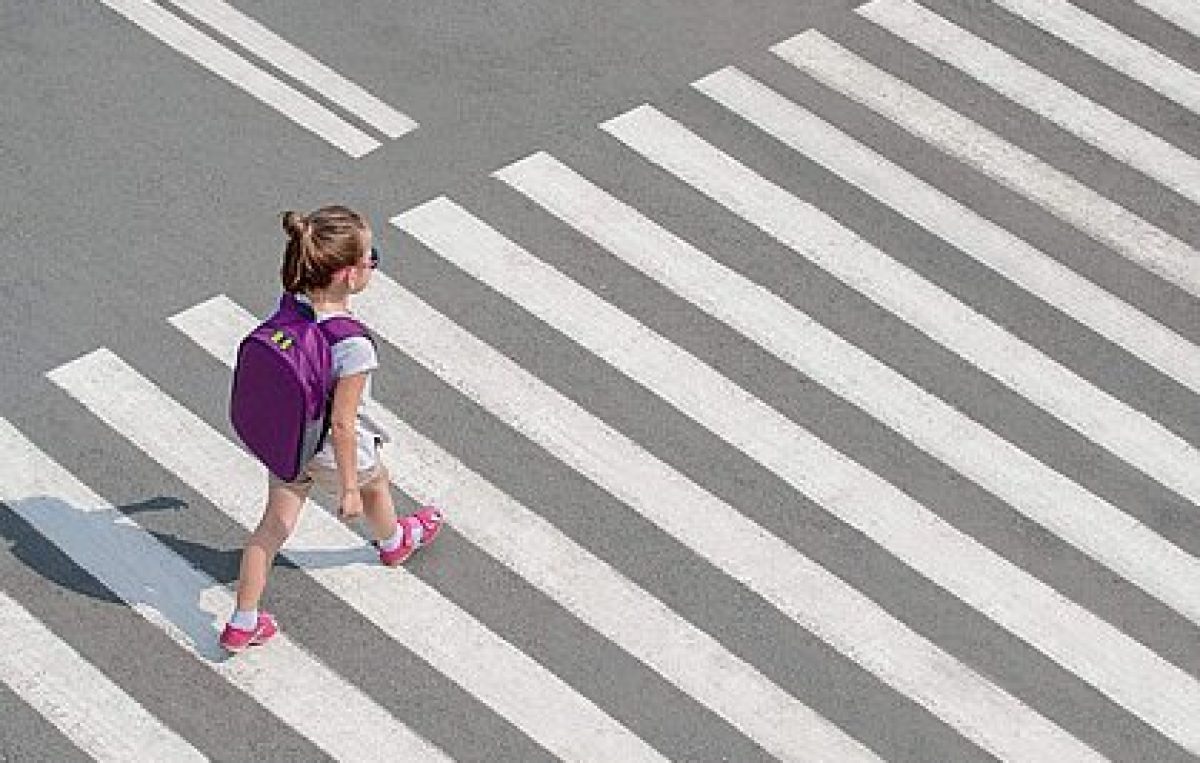 Ein Mädchen mit Rucksack überquert aufmerksam einen Zebrastreifen.
