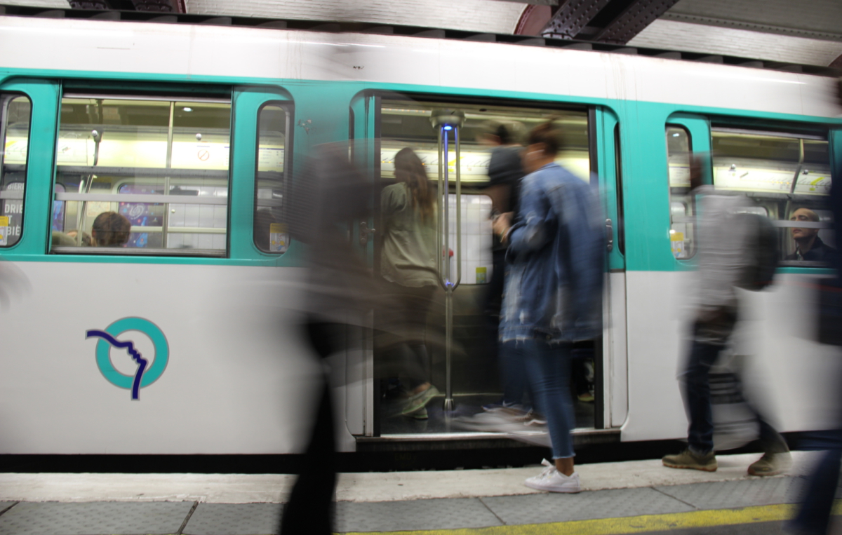 Menschen steigen in eine U-Bahn ein, während andere unscharf vorbeigehen; am Bahnsteigrand ist die gelbe Sicherheitslinie sichtbar.