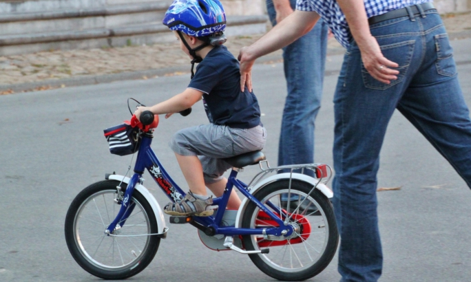 Eltern üben mit Kind Fahrrad fahren